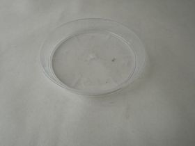Un dessous de verre rond transparent en plastique est posé sur un fond gris structuré.