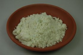 Braune Keramikschale gefüllt mit weißem, körnigem Material, das mit vereinzelten blauen Flecken durchsetzt ist. Das Ganze liegt auf einer grauen Oberfläche.