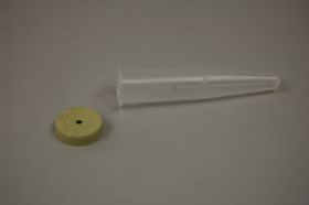 A translucent, conical container lies horizontally on a grey surface. A flat, yellow disc with a hole in the centre lies to the left of it.
